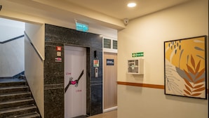 Um saguão de hotel com escadas, um sinal de saída de incêndio, um sinal de primeiros socorros e uma obra de arte emoldurada na parede.