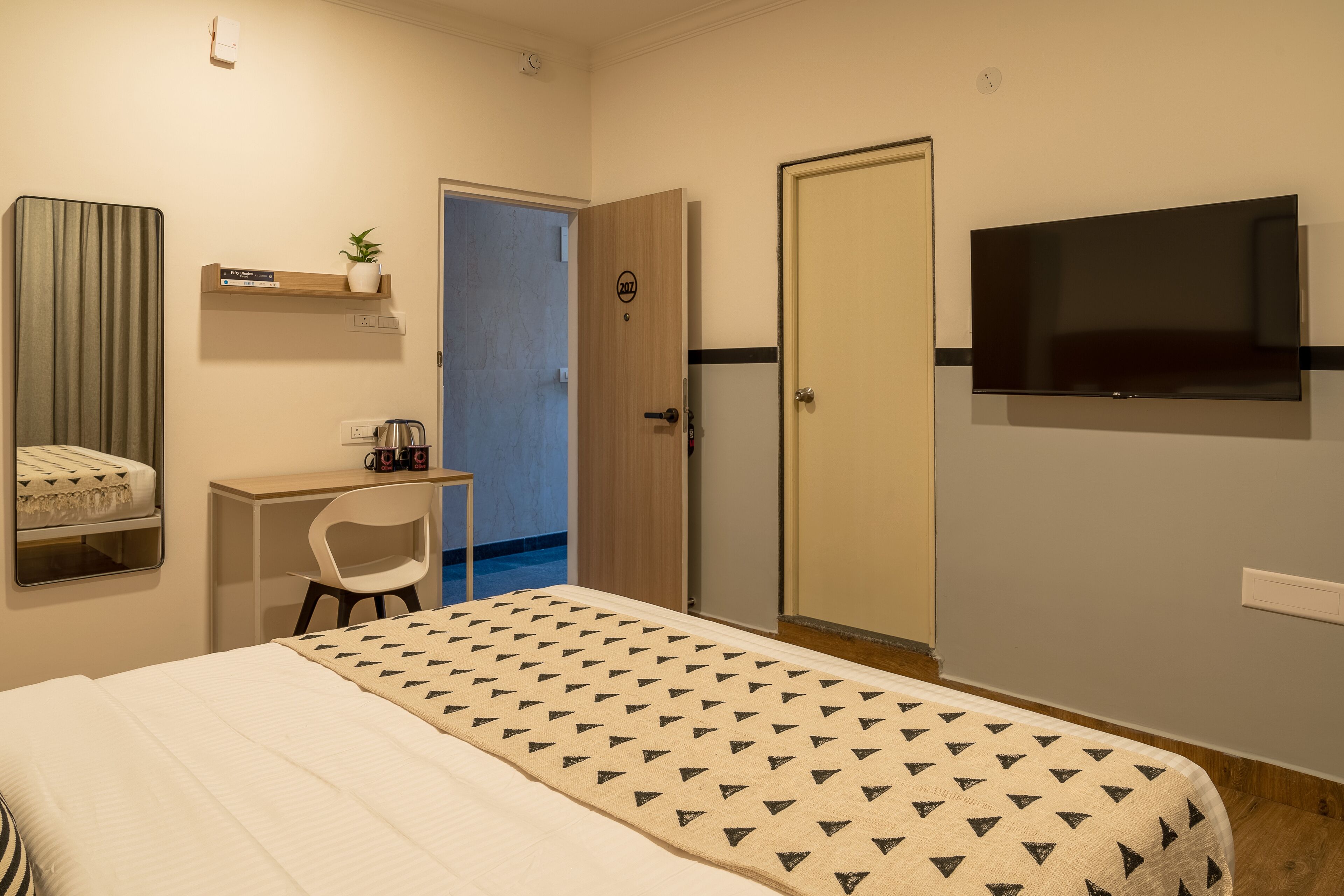 A hotel room with a bed, a desk, a chair, a TV, and a wardrobe.