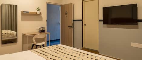 A hotel room with a bed, a desk, a chair, a TV, and a wardrobe.