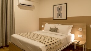 Cama bem arrumada com colcha estampada, mesa de cabeceira com abajur e um quadro na parede.