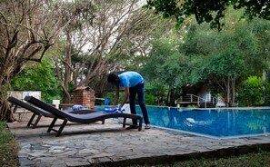 Un espace aménagé au bord de la piscine, avec un fauteuil de relaxation, une structure en briques et une personne qui nettoie la piscine.