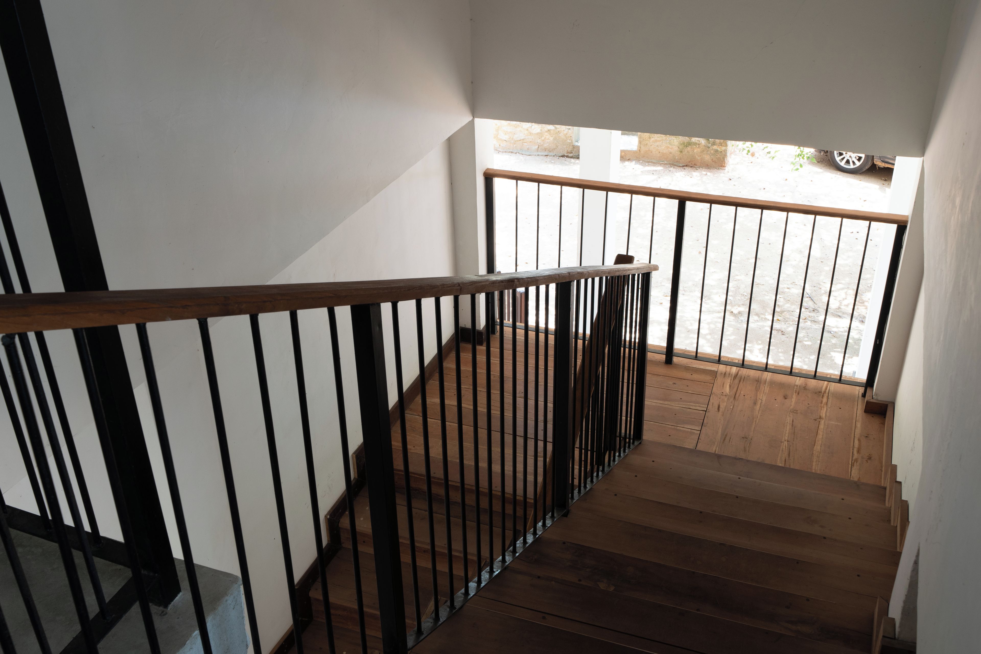 Una escalera de madera con barandas negras que lleva a un balcón con vista a la calle.