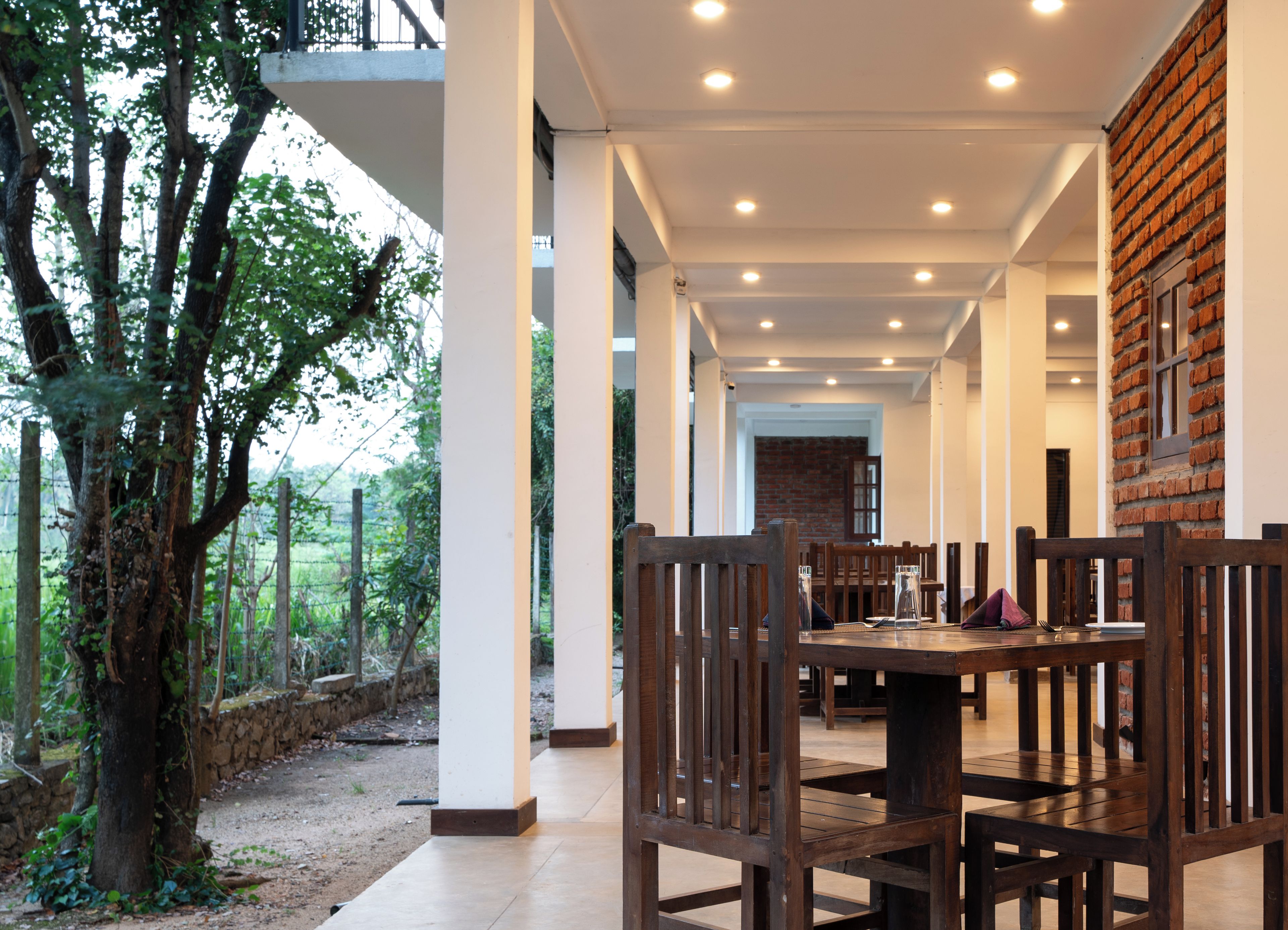 A dining area with wooden tables and chairs, a brick wall, and a view of trees.