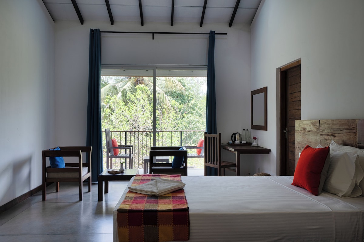 Une chambre d’hôtel avec un lit, un banc, une table, des chaises et une vue sur l’extérieur.