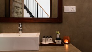 Une salle de bain avec un lavabo blanc, un miroir, un escalier en bois et un luminaire fixé au mur.