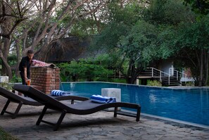 A pool area with lounge chairs, a brick structure, and a staircase leading to a building.