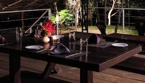 Un espace de restauration en plein air avec une table dressée pour deux personnes, comprenant des assiettes, des couverts, des verres et une bougie.