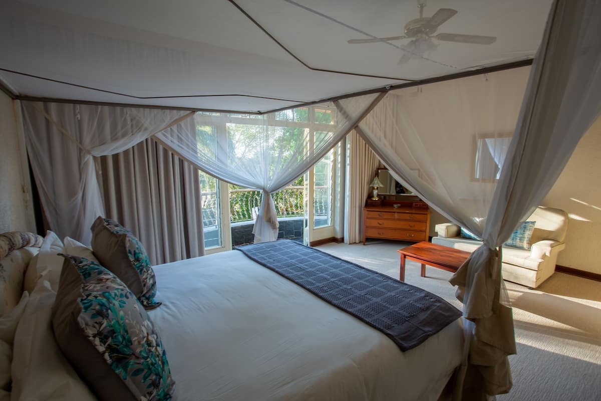 A bedroom with a large bed, a canopy, a ceiling fan, and a view of the outdoors.