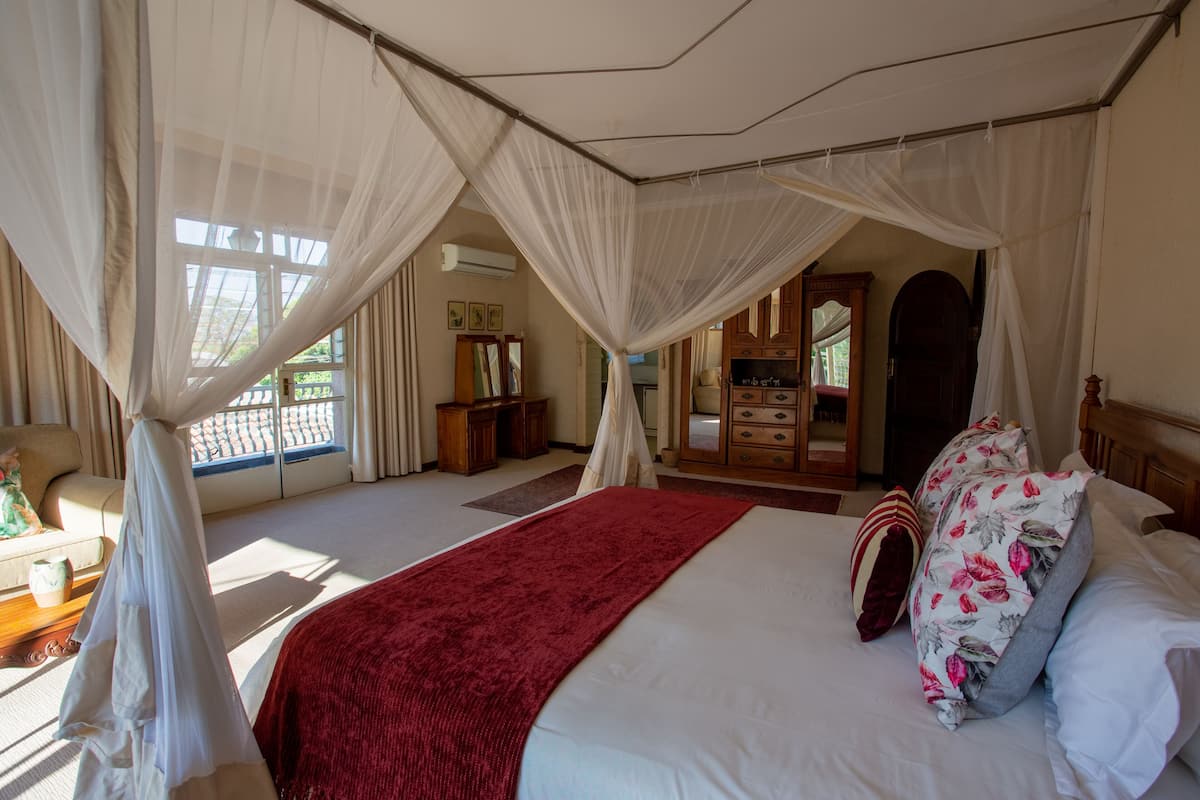 A bedroom with a large bed, white curtains, a red blanket, and a wooden dresser.