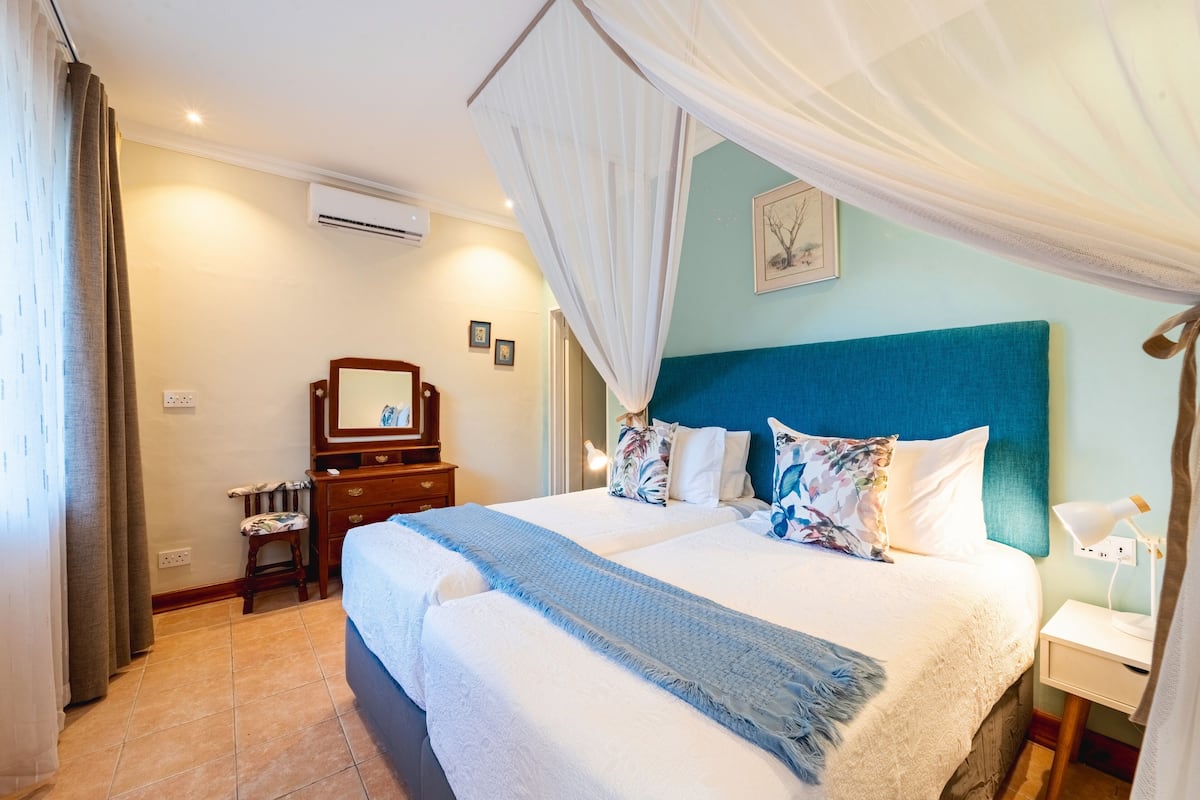 A neatly arranged bedroom with a large bed, a nightstand, a dresser, and a mirror.