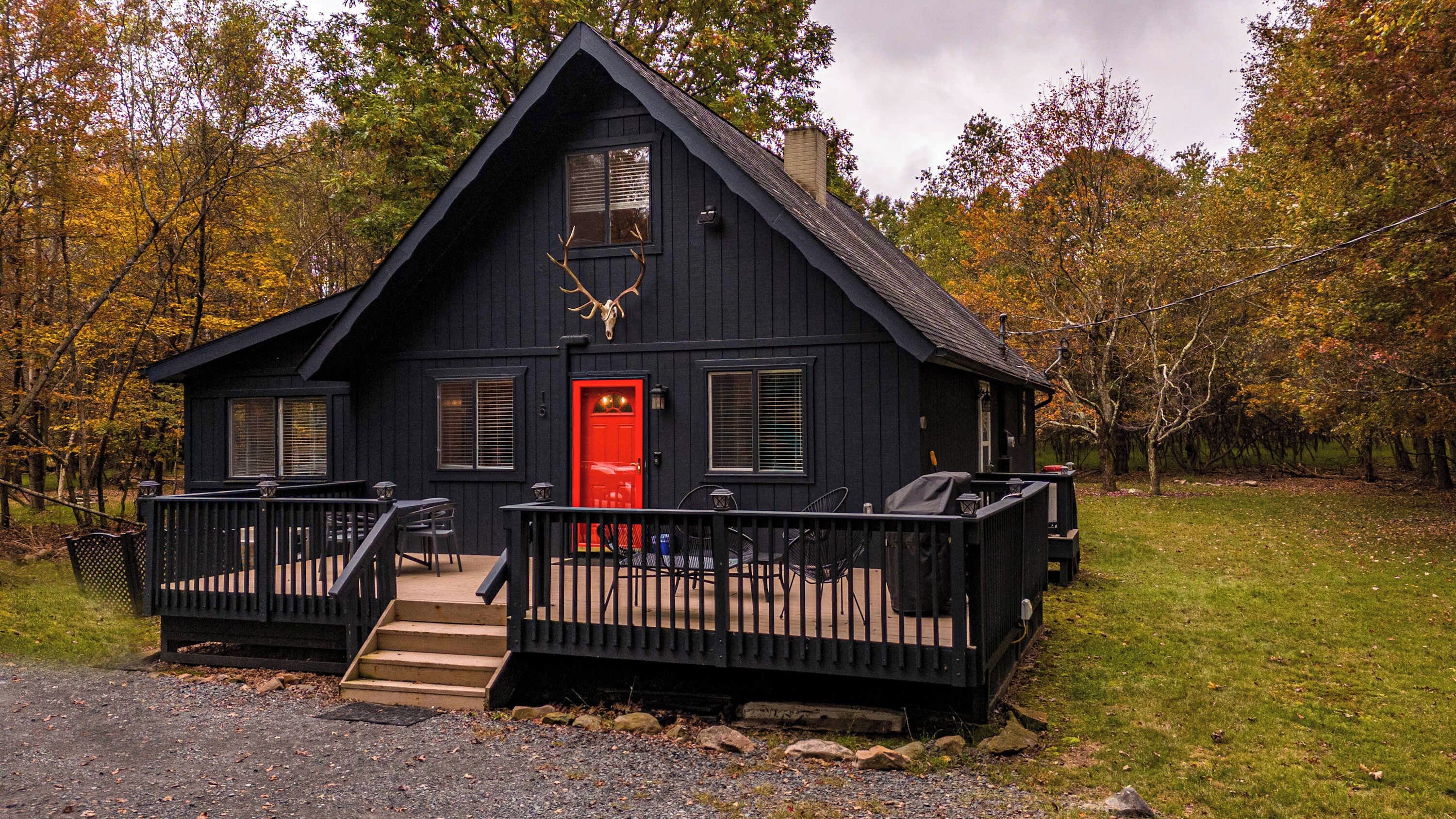 A black cabin with a red door, a front porch, and a deer skull decoration.