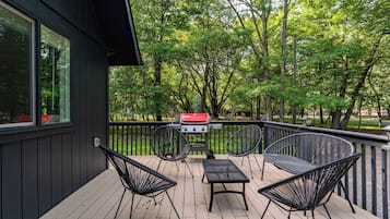 Een terras met een barbecue, twee stoelen en een tafel.