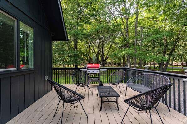 A deck with a grill, two chairs, and a table.