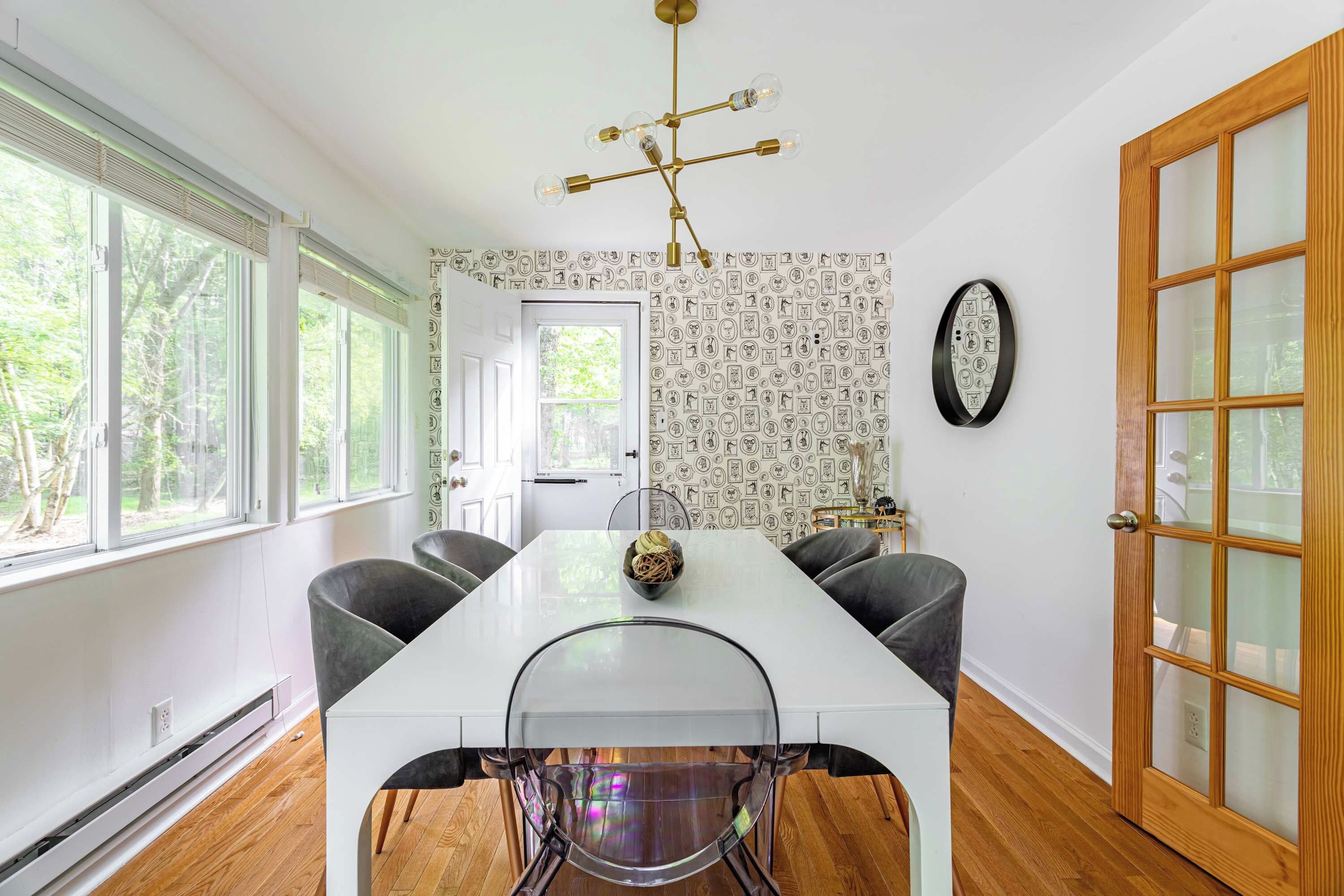 A dining area with a white table, four chairs, a chandelier, and a patterned wallpaper.