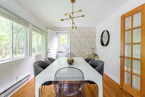 Un comedor con una mesa blanca, cuatro sillas, una araña y un papel tapiz estampado.