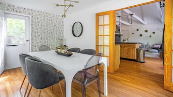 A modern dining area with a white table and grey chairs, a kitchen in the background, and a wooden floor.