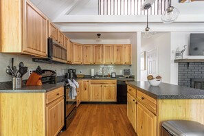 Una cocina con armarios de madera, microondas, estufa y lavavajillas. Hay una encimera con un lavabo y una ventana encima.