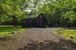 A cabin with a gravel driveway, surrounded by trees.