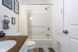 Een badkamer met een wit toilet, een wastafel met granieten blad, een badkuip en een douchegordijn.