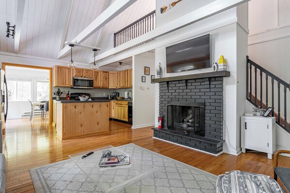 A spacious living area with a fireplace, wooden flooring, and a kitchen with wooden cabinets.