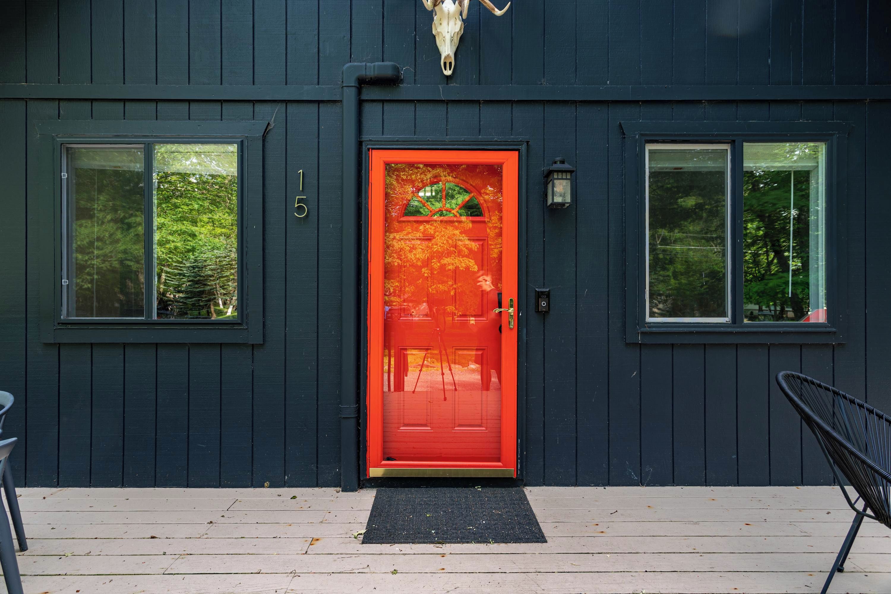 A dark blue building with a red door, numbered 15, and two windows.