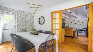 A modern dining area with a white table and grey chairs, a kitchen in the background, and a wooden floor. - Stag Chalet: Summer Retreat | 3BD | Pet Friendly (Albrightsville)