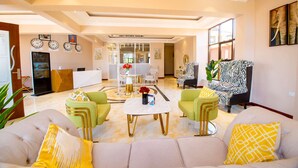 A spacious living area with a sofa set, a coffee table, and a zebra-patterned chair. There are clocks on the wall and a large window providing natural light.