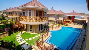 A residential property with a swimming pool, multiple houses, and a landscaped garden.