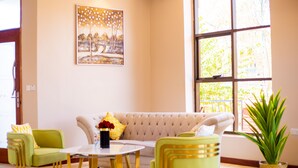 A modern living room with a beige sofa, green armchairs, a round coffee table, and a large window with natural light.