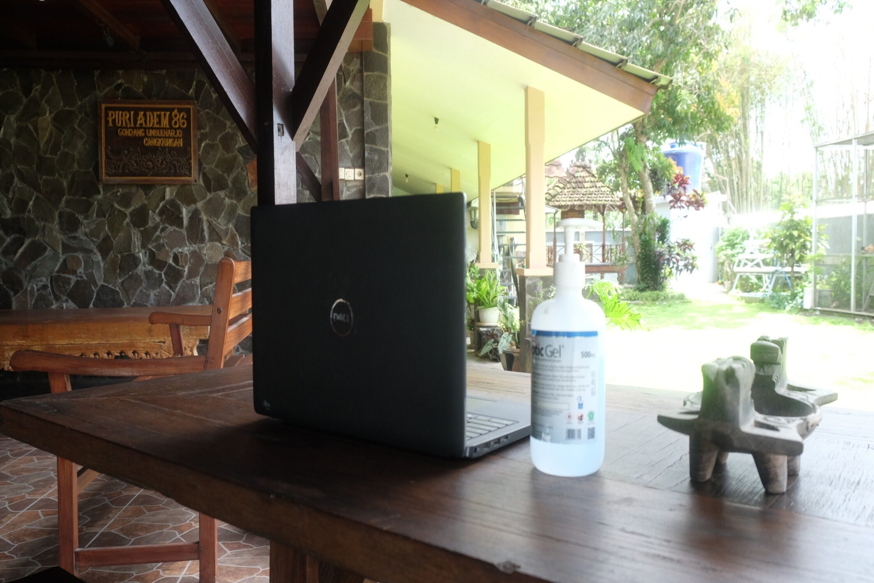 A laptop on a wooden table with a stone wall and a bench in the background.