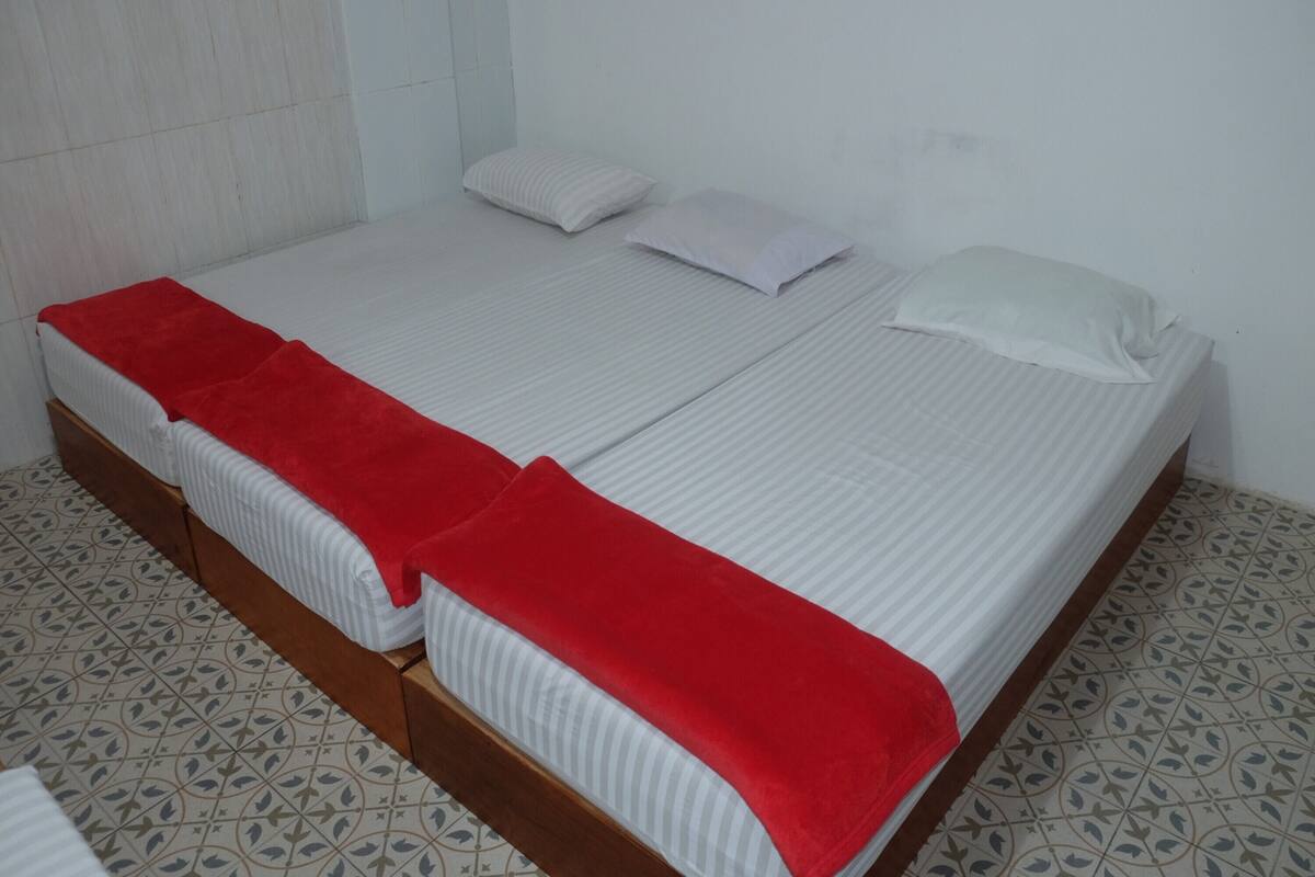 Cama doble con una colcha roja, almohadas blancas y un cabecero de madera.