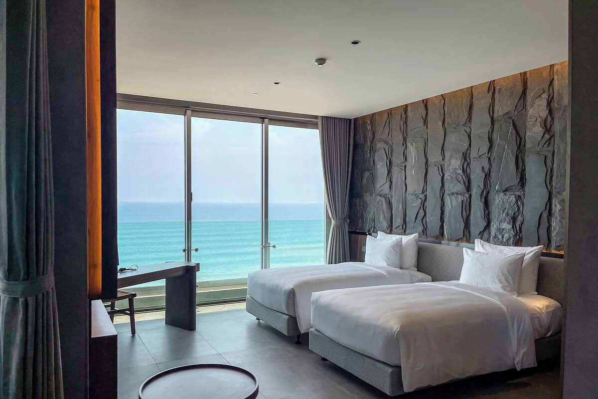 A hotel room with a large bed, a small table, and a view of the ocean.