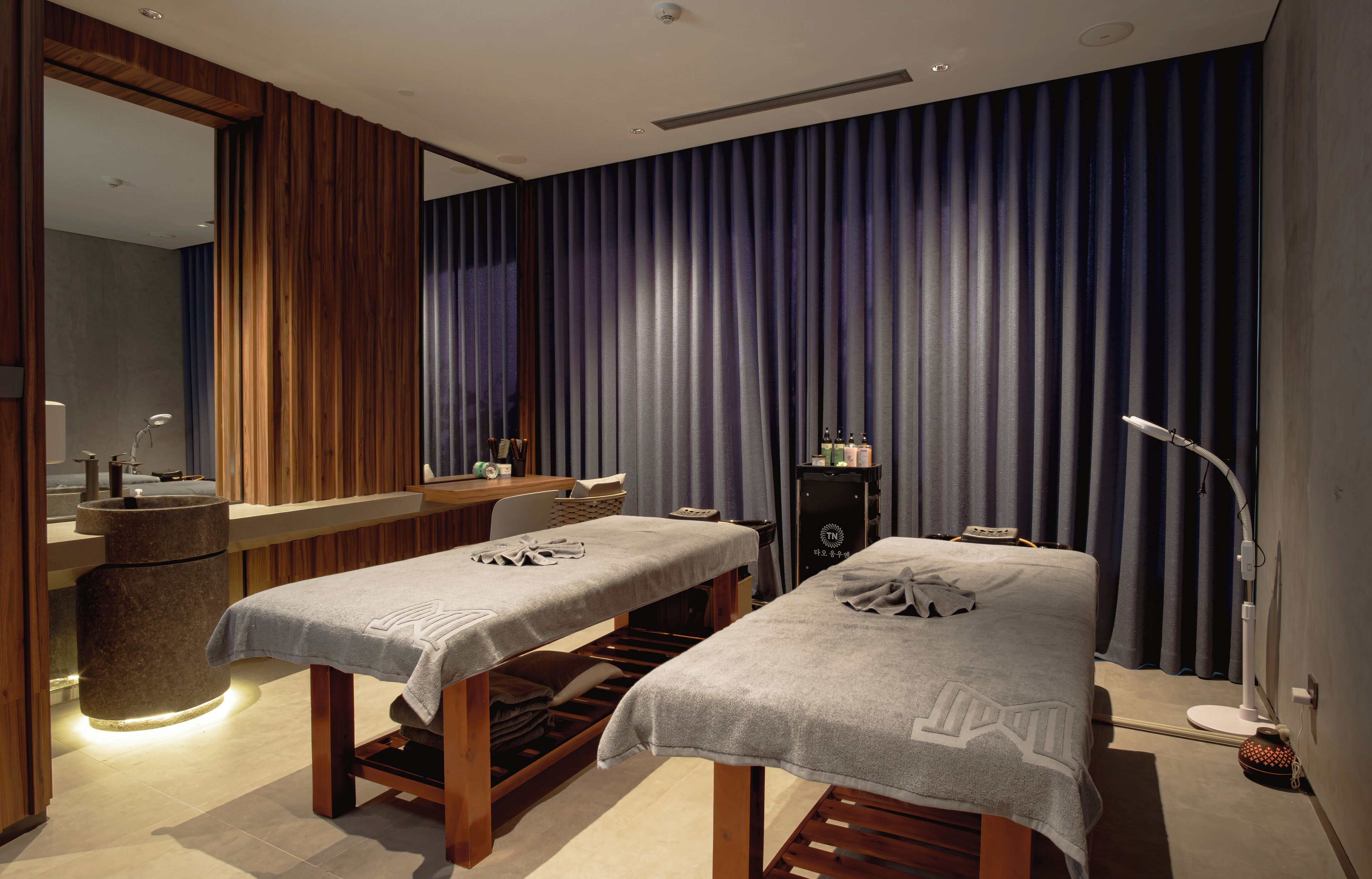A spa room with two massage tables, a reception desk, and a large mirror.