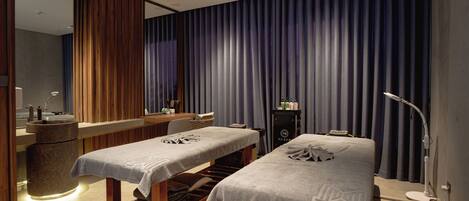 A spa room with two massage tables, a reception desk, and a large mirror.