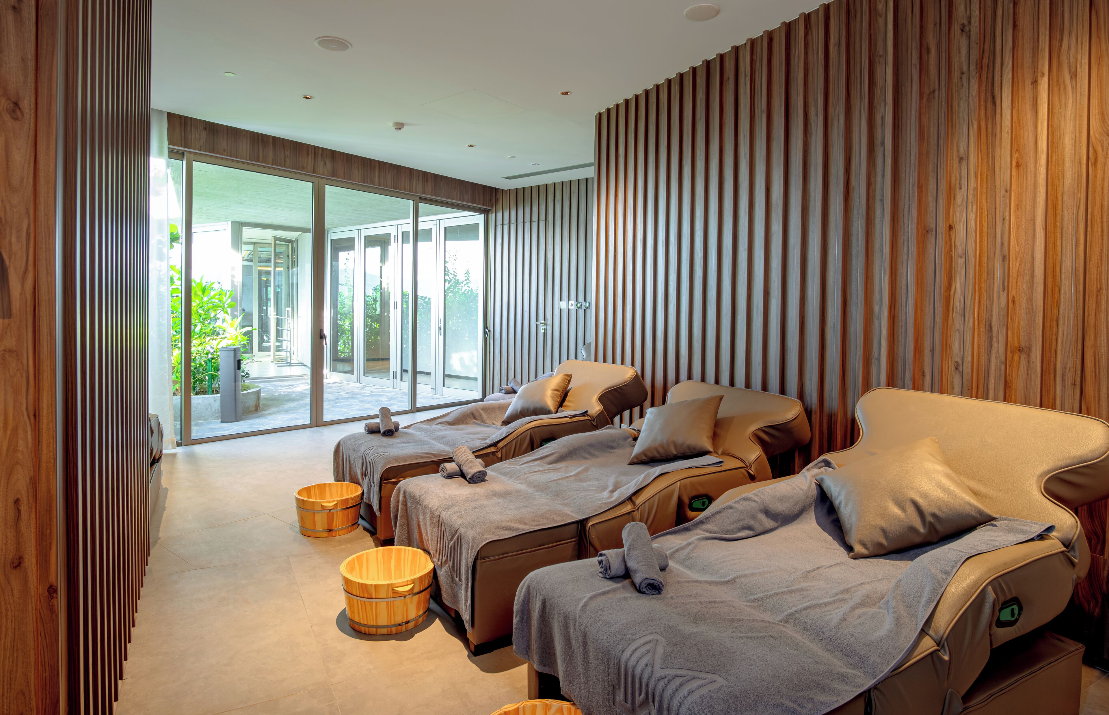 A spa room with three massage beds, wooden accents, and a view of greenery outside.