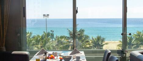 A dining area with a table set for two, overlooking a beach with palm trees and the ocean.