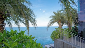 A poolside view with a clear view of the sea, surrounded by lush greenery and palm trees. - M HOTEL DANANG (Da Nang)