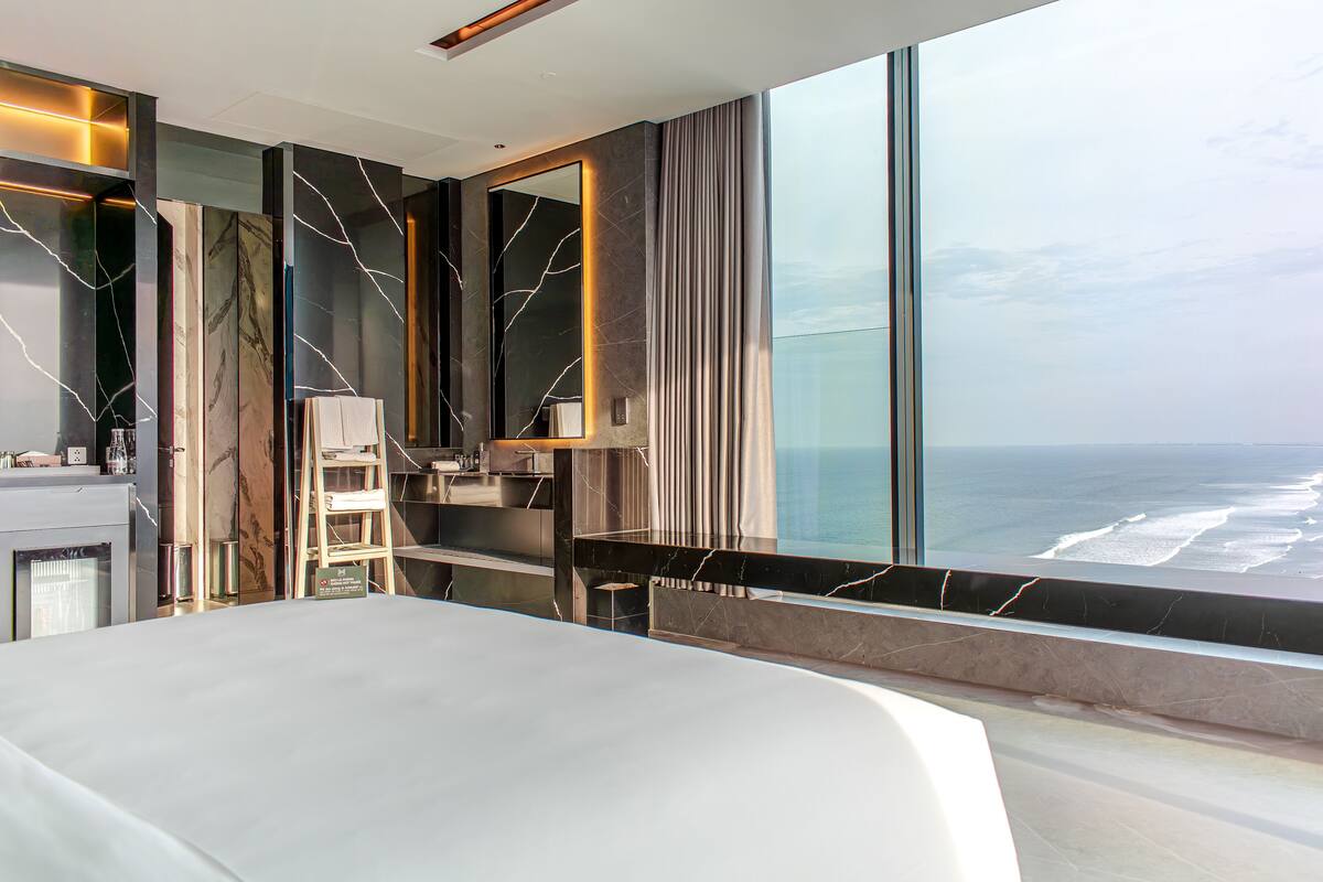 A modern hotel room with a large bed, a desk, and a view of the ocean.