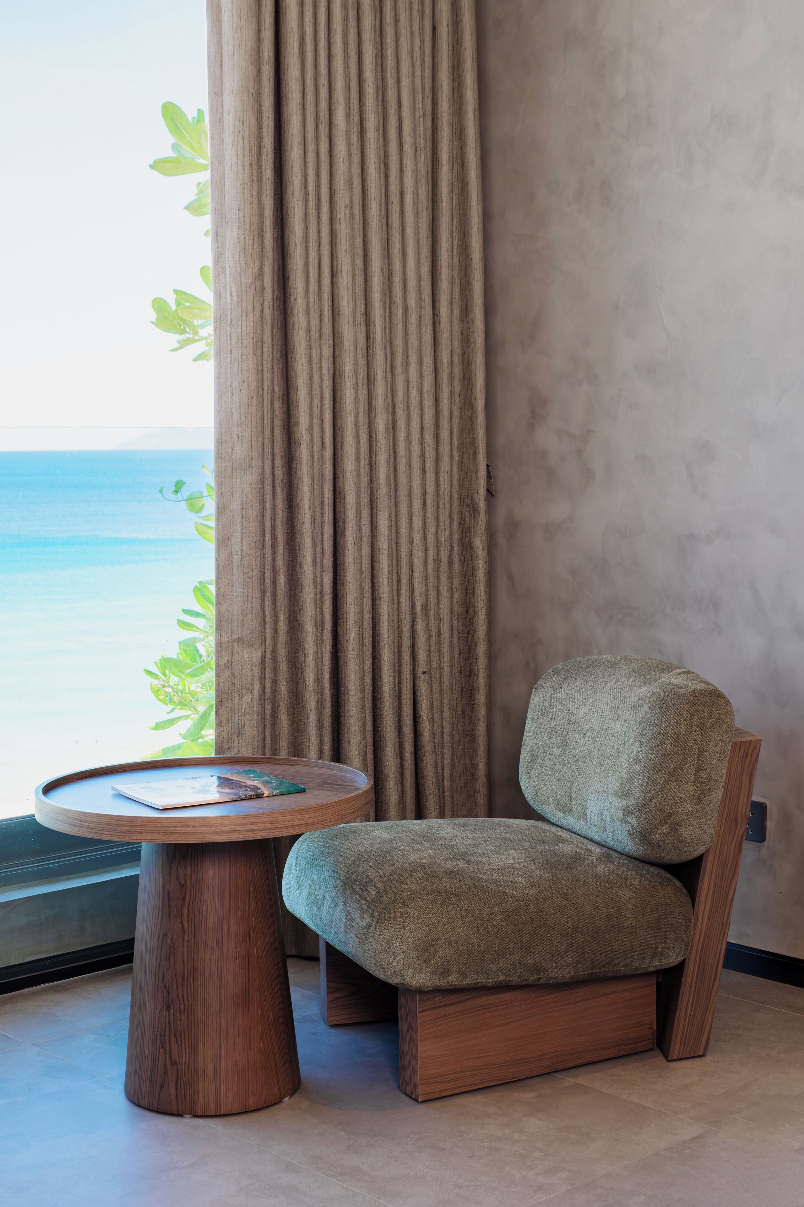 A room with a view of the sea, a round wooden table, and a cushioned chair.
