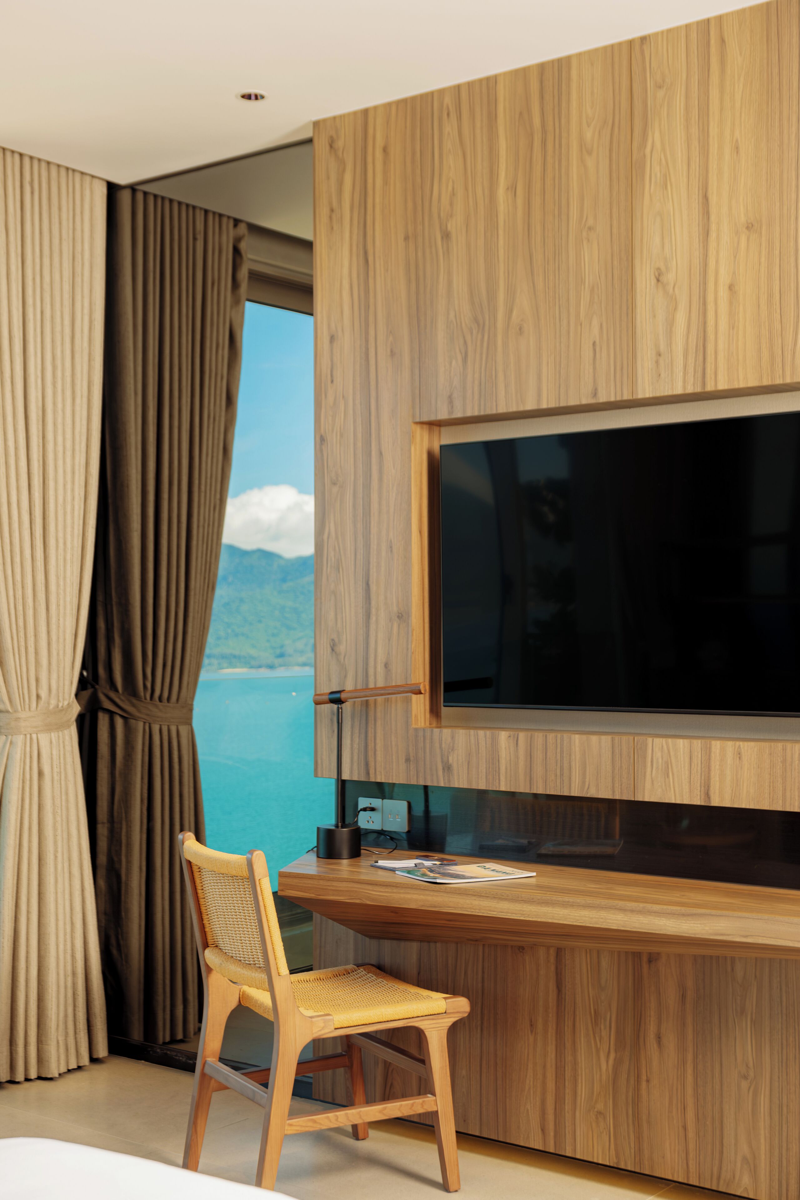 Una habitación moderna con un escritorio de madera, una silla, un televisor de pantalla plana y vistas al mar.