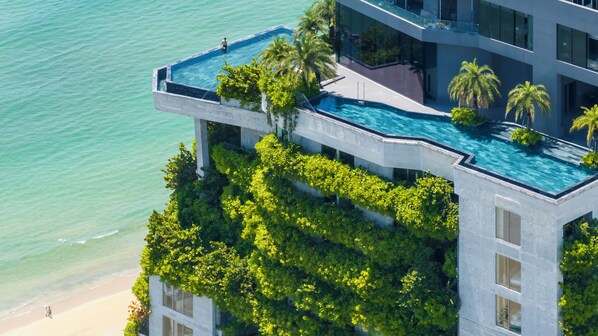 A modern hotel with a rooftop infinity pool overlooking the ocean, lush greenery, and a beach view. - M HOTEL DANANG (Da Nang)