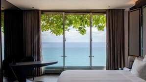 A hotel room with a large bed, a desk, and a view of the sea through floor-to-ceiling windows. - M HOTEL DANANG (Da Nang)