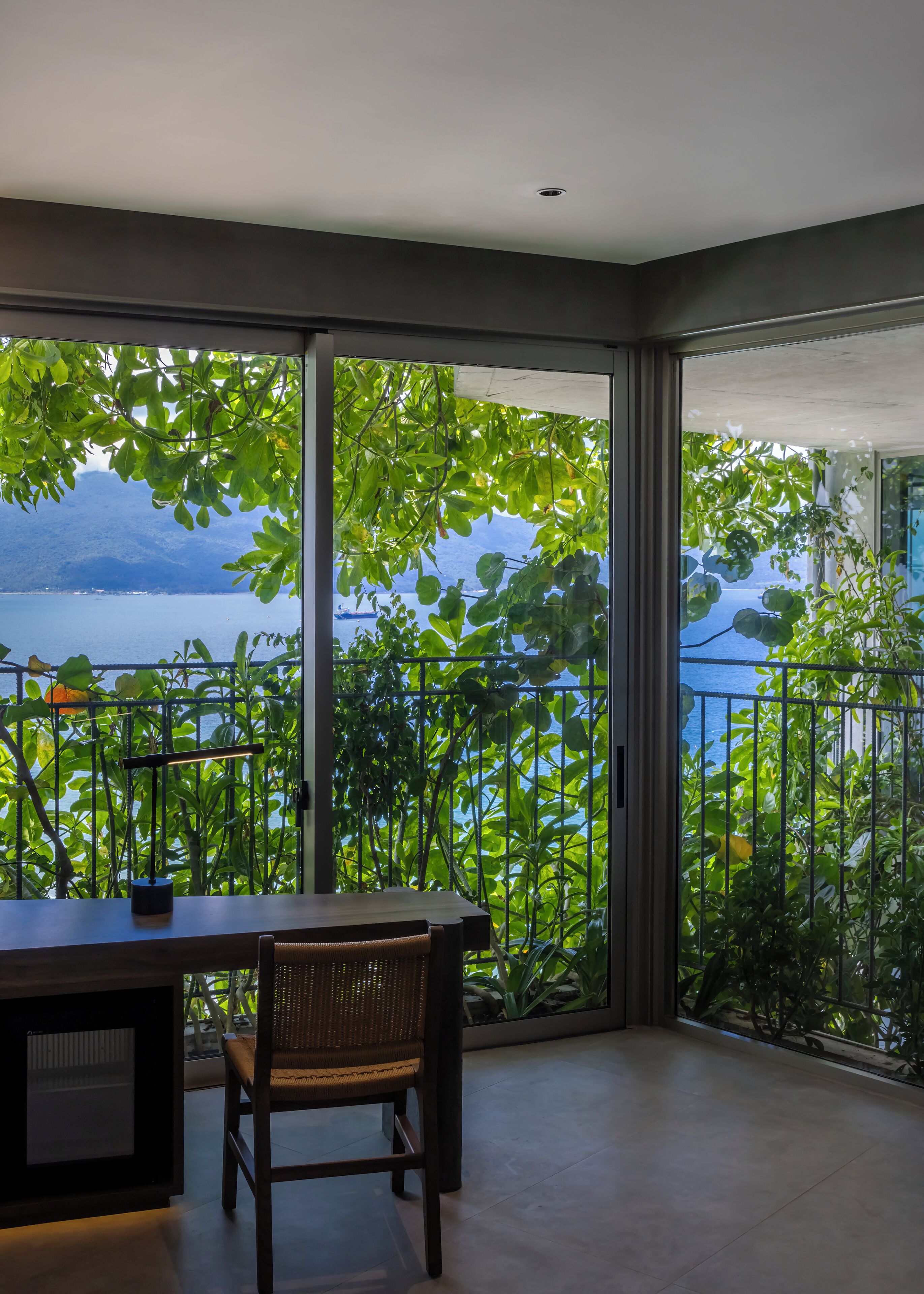 A balcony with a view of a lake and mountains, a table, and a chair.