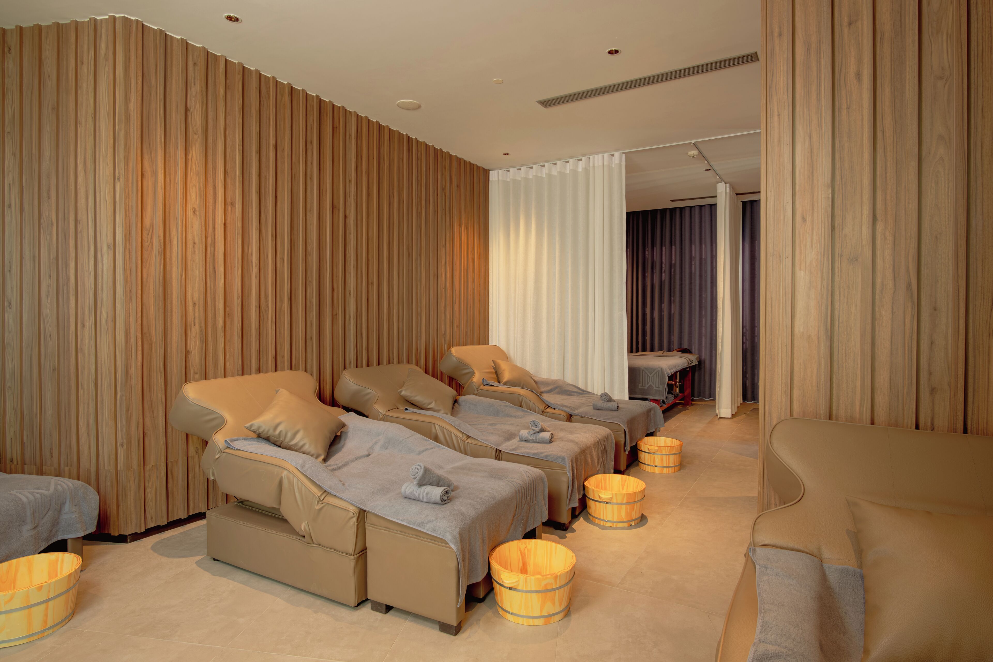 A spa room with three massage beds, wooden walls, and a large window with curtains.