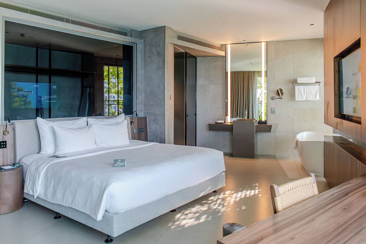 A modern hotel room with a large bed, a bathroom with a bathtub, and a seating area.