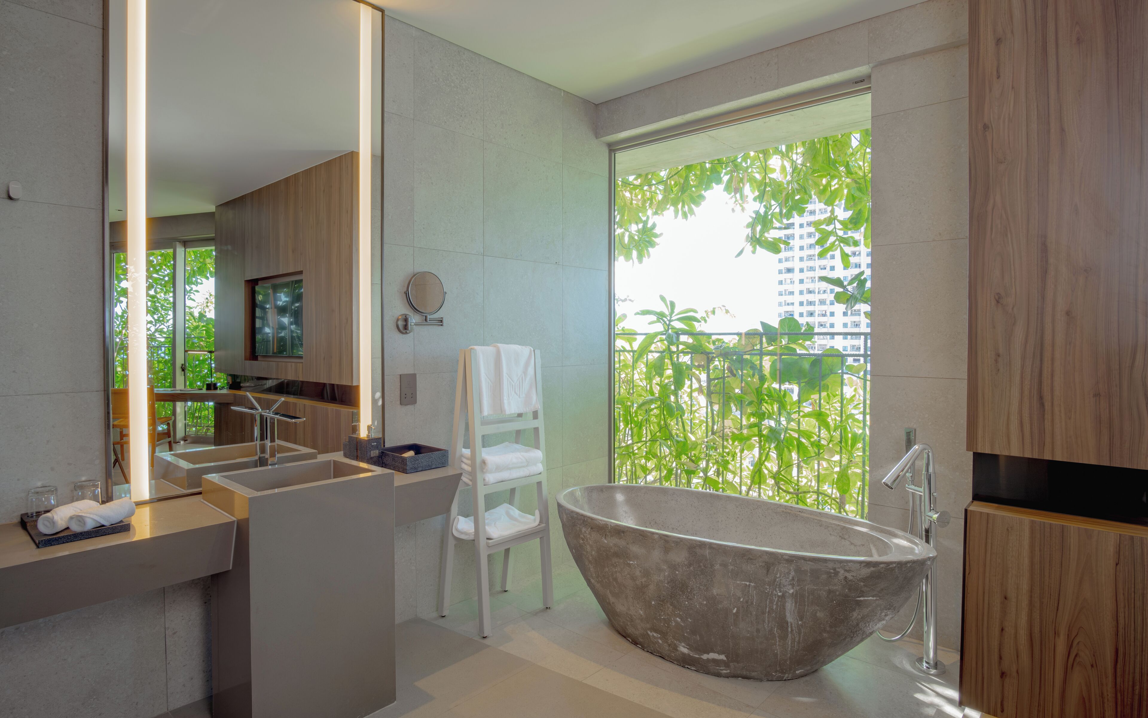 A modern bathroom with a freestanding bathtub, a large mirror, and a view of greenery outside.