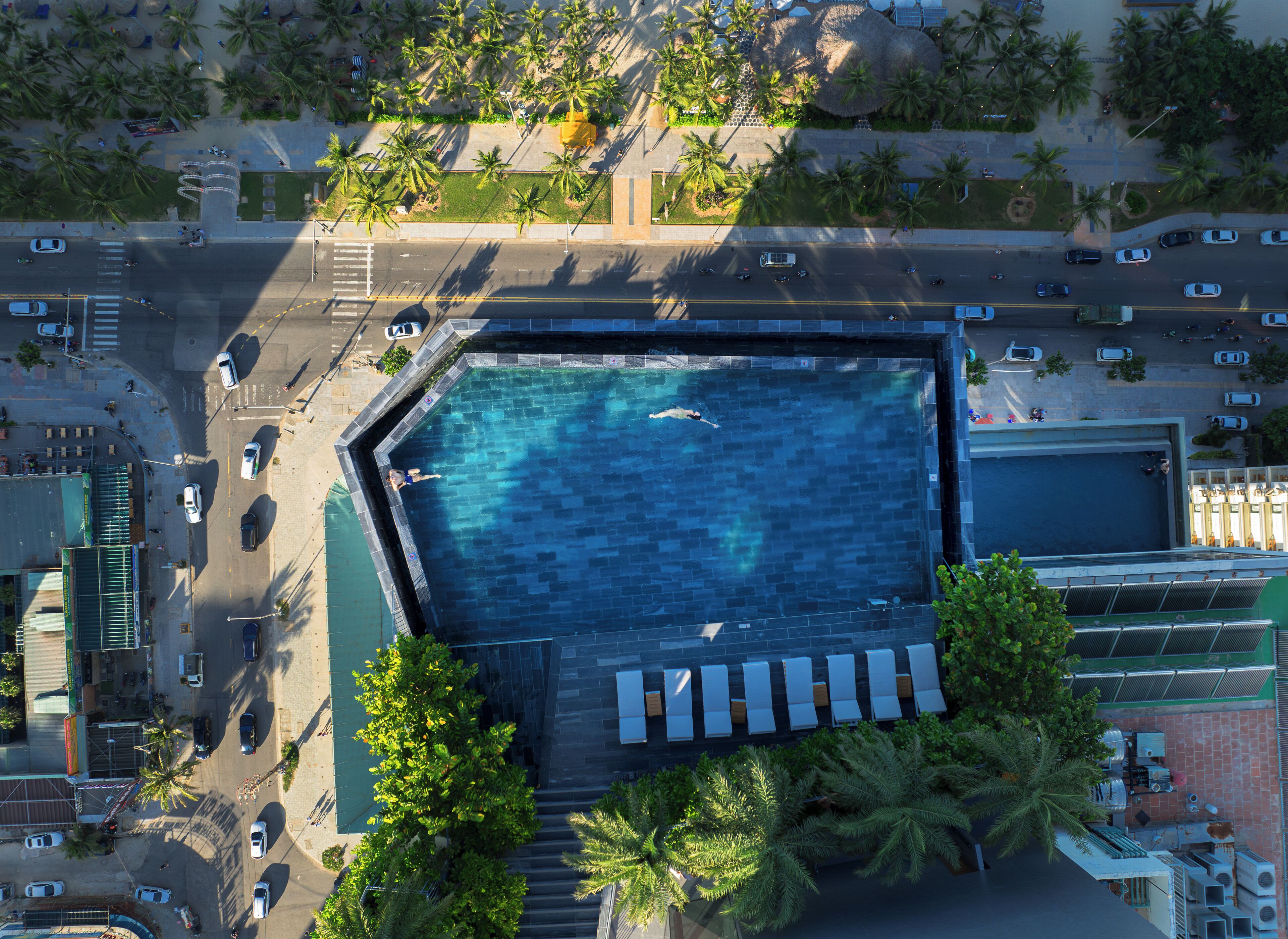 An aerial view of a swimming pool surrounded by palm trees and parked cars.