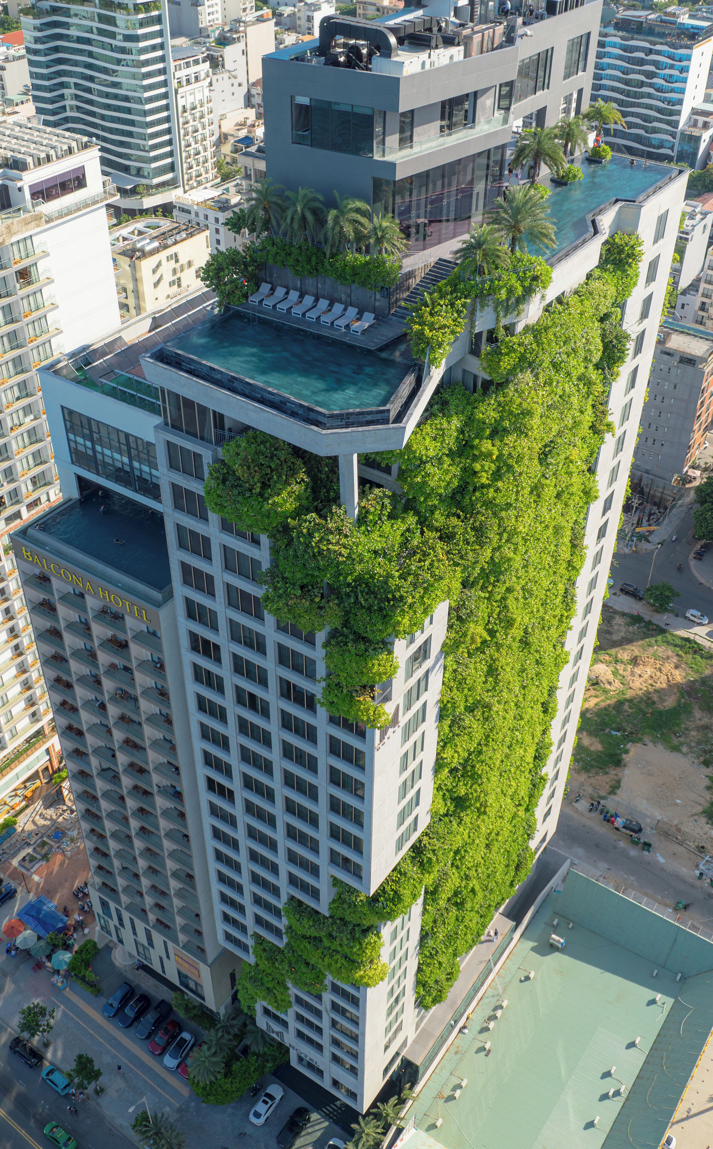 A high-rise building with a rooftop pool and a balcony with lush greenery.