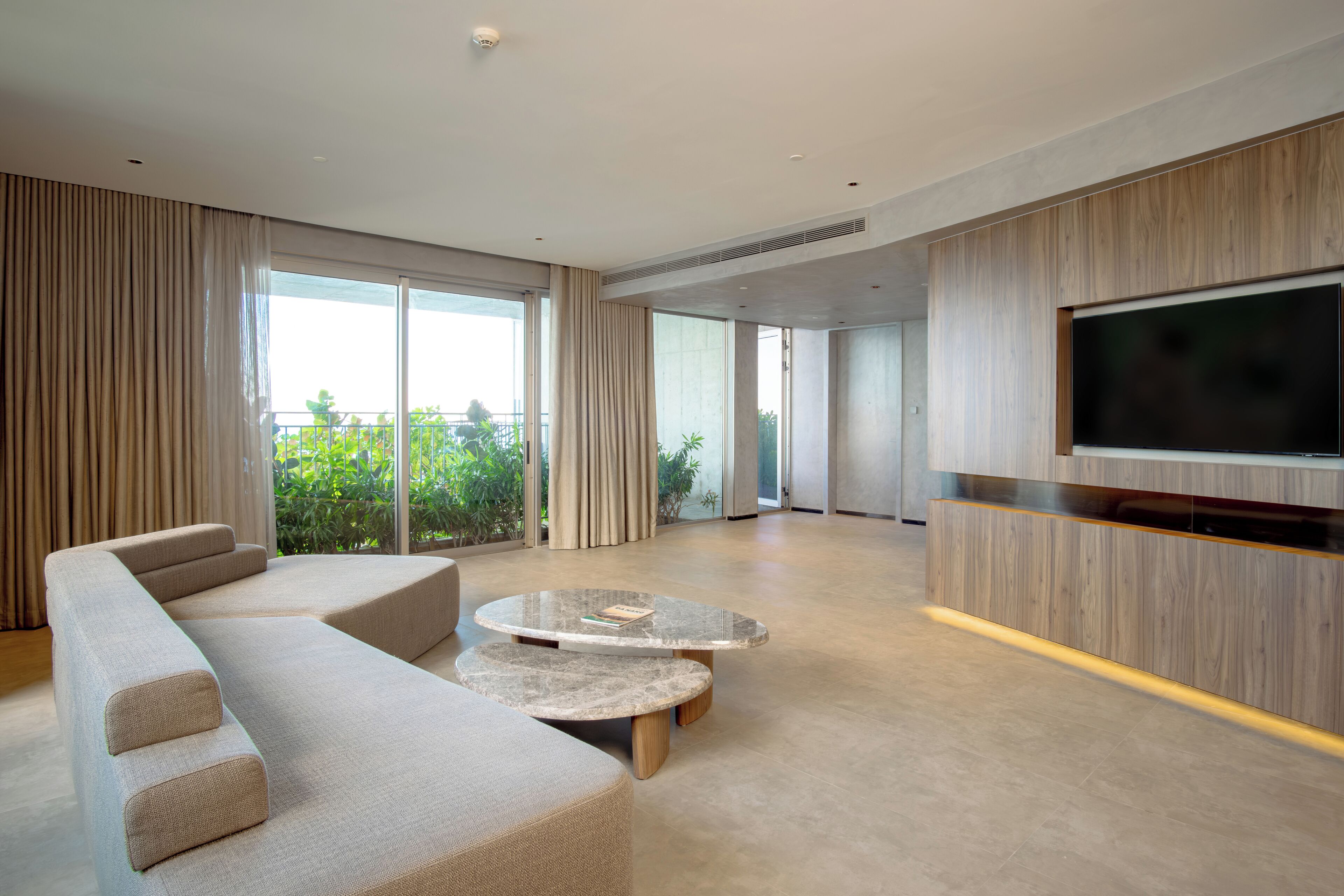 Un salon moderne avec un grand canapé d’angle, une table basse en marbre et un téléviseur à écran plat fixé sur un meuble en bois.
