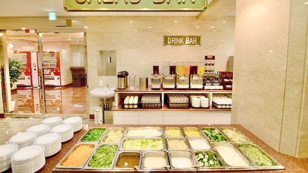 Una barra de ensaladas con diversas opciones de comida y una barra de bebidas en un ambiente limpio e iluminado.